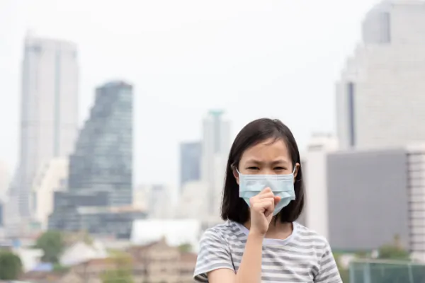 Menina oriental de máscara em meio à poluição representando os danos das alterações climáticas à saúde infantil